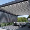 Terasoje įrengta tamsaus rėmo pergola su atviru stogu ir lauko roletais