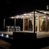Tamsi tentinė pergola namo terasoje su apšvietimu ir uždaru stogu naktį